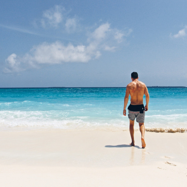 person walking in beach with white sane and blue water