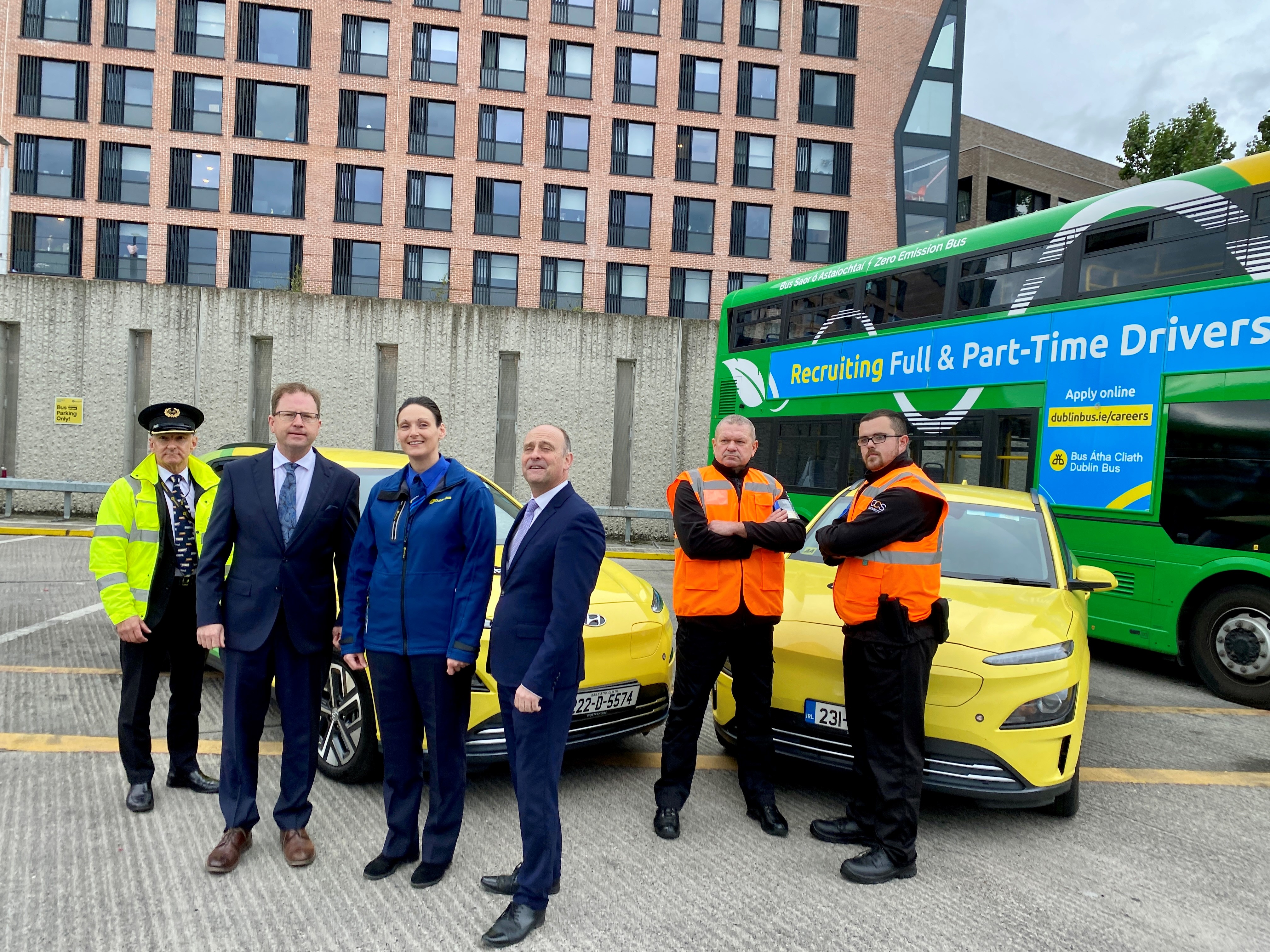 Image of Billy Hann (CEO), a female bus driver, our Safer Journey Team and Chief Inspector, all standing in front of a Dublin Bus and two green and yellow Dublin Bus cars in Broadstone bus depot